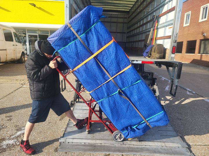 Mover wheeling a blanket-wrapped appliance onto a truck liftgate (pickup and delivery services) by Moving Pros CLE